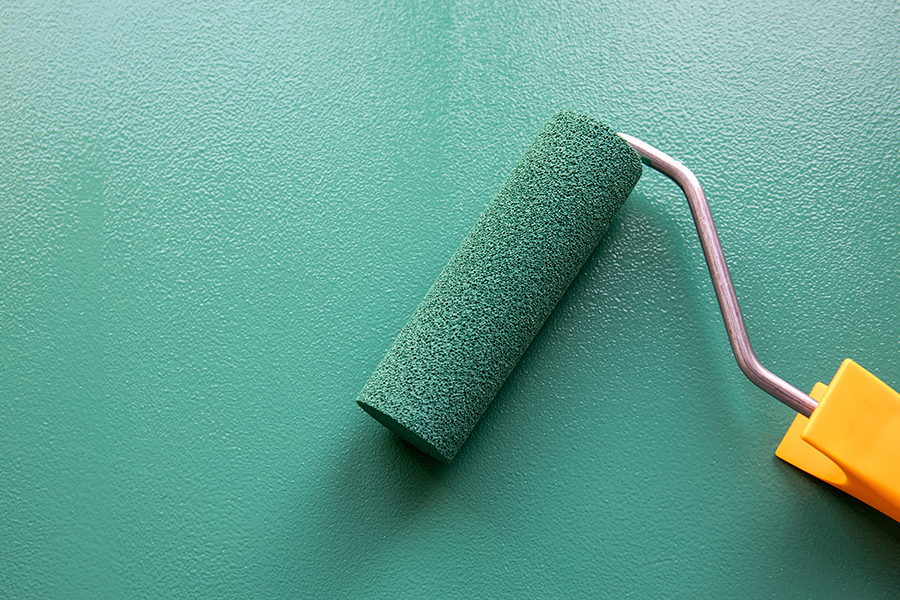 Paint roller applying consistent green commercial paint color for multi-location brand standardization